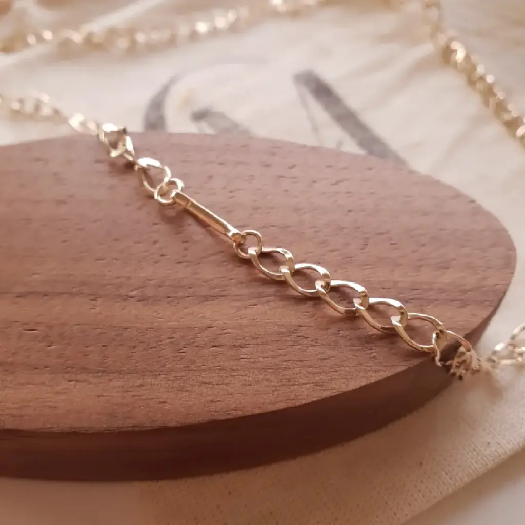 Pulseira delicada em ouro sobre suporte de madeira