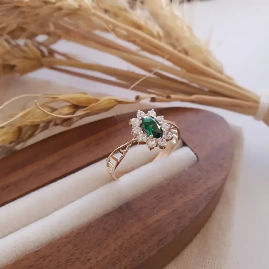 Anel com pedra verde e diamantes sobre suporte de madeira